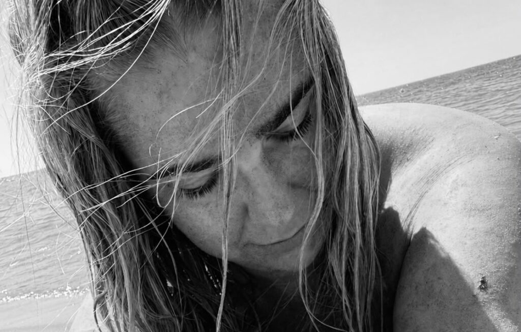 Ein schwarz weiss Bild von einer Frau, die am Strand ist und sich eine Muschel auf den Arm legt.