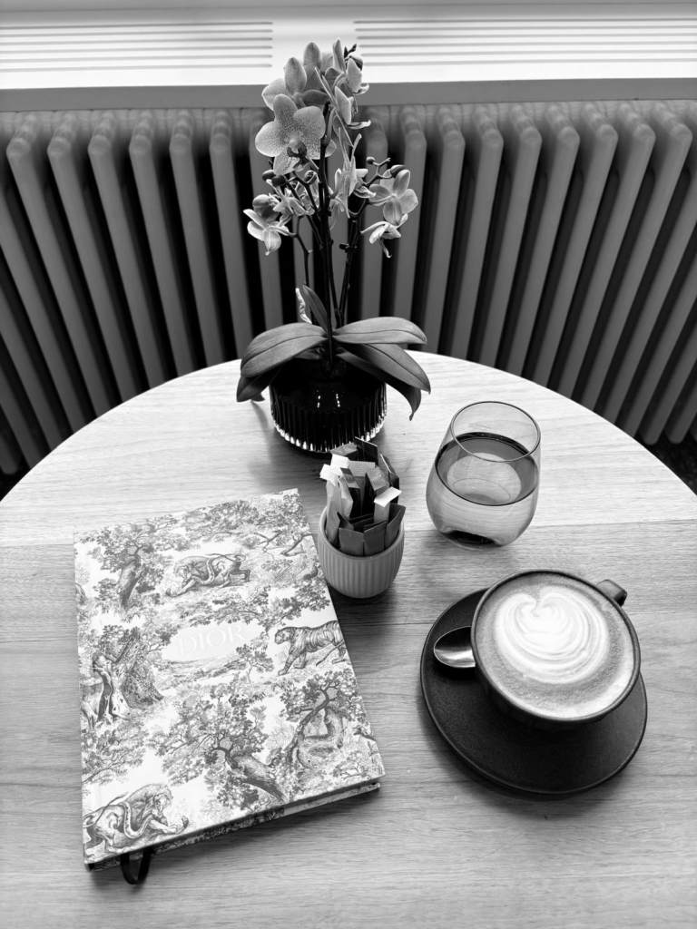 Tisch mit einem Kaffe, einem Glas Wasser, einer Blume und einem Journal darauf